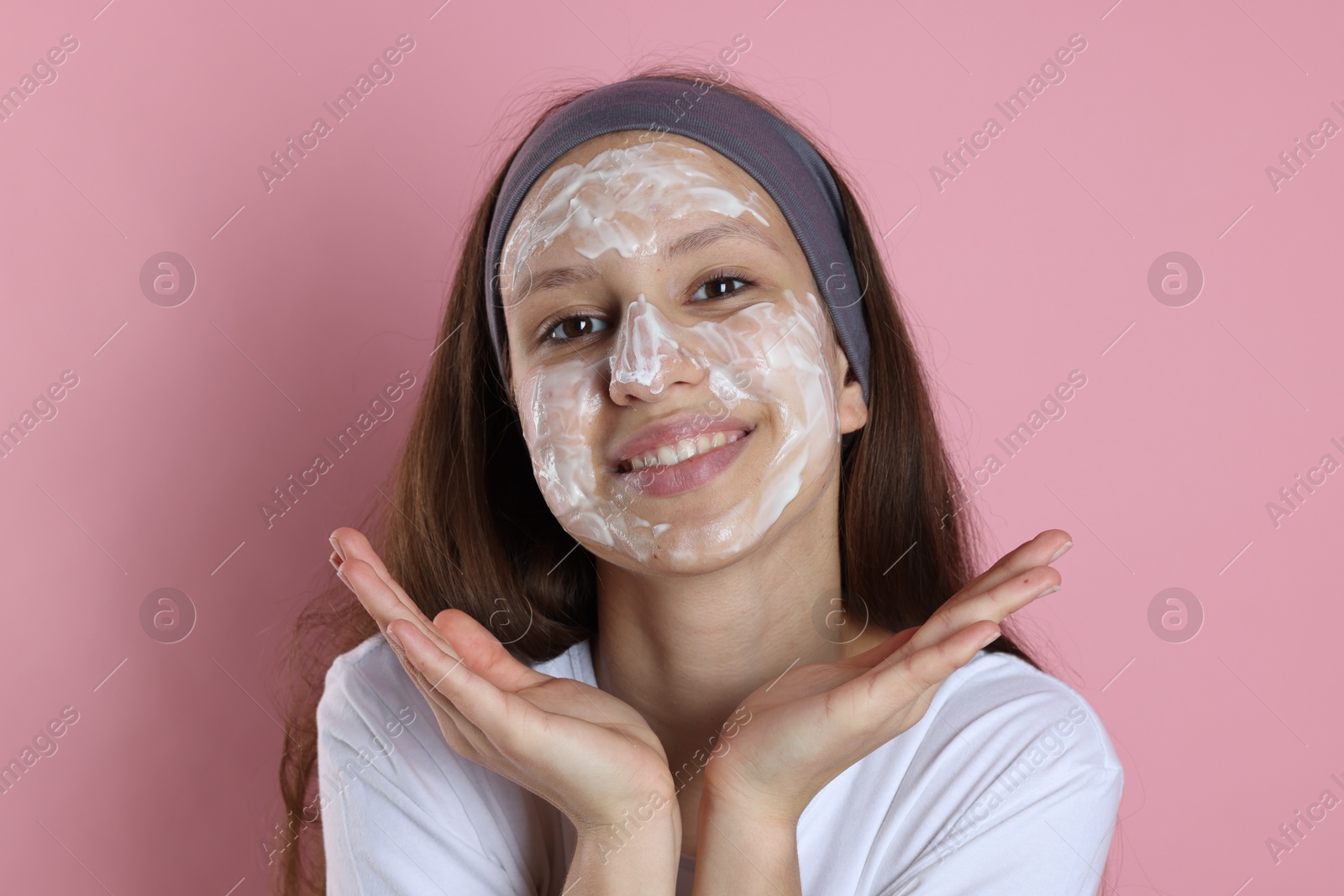 Photo of Teenage girl with cream on her face against pink background. Acne treatment