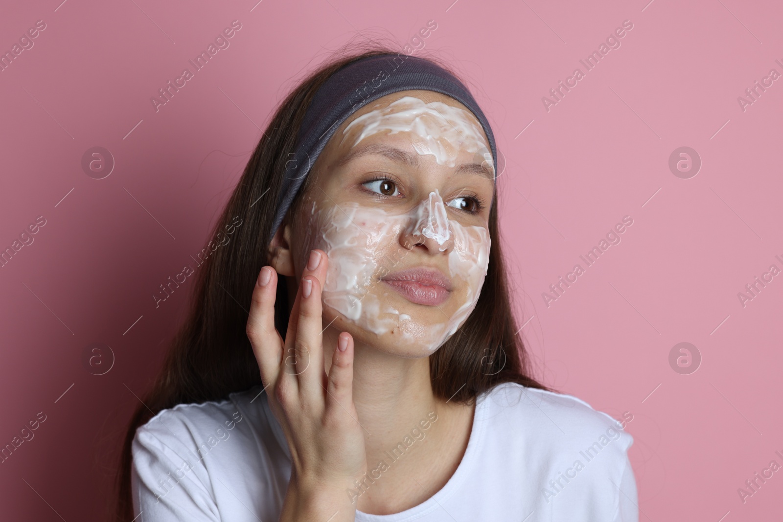 Photo of Teenage girl with cream on her face against pink background. Acne treatment