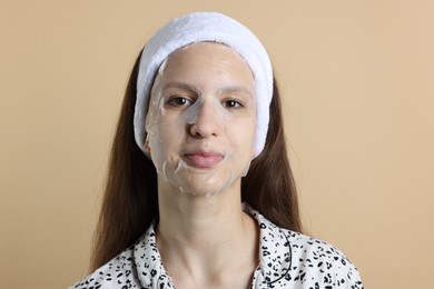 Photo of Teenage girl with sheet facial mask on beige background. Acne treatment