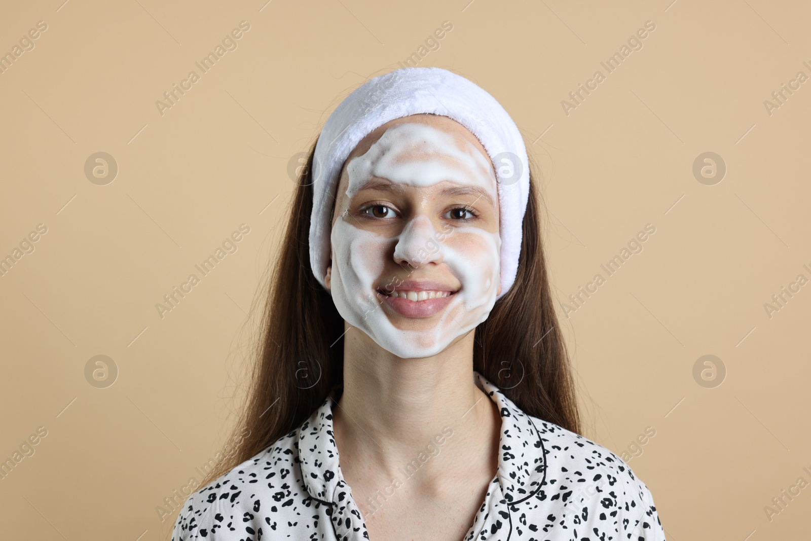 Photo of Teenage girl with cleansing foam on her face against beige background. Acne treatment