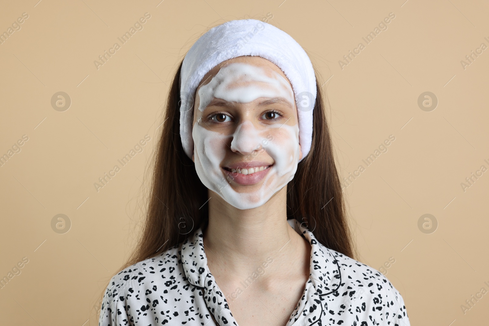 Photo of Teenage girl with cleansing foam on her face against beige background. Acne treatment