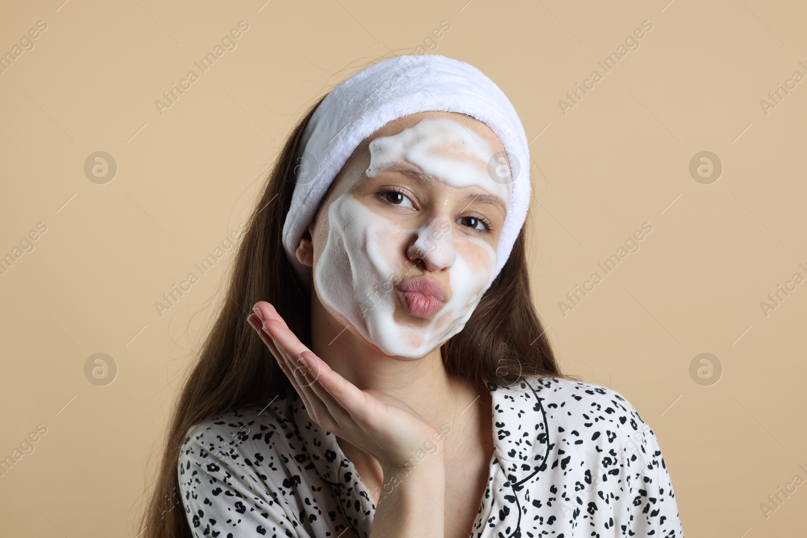 Photo of Teenage girl with cleansing foam on her face against beige background. Acne treatment