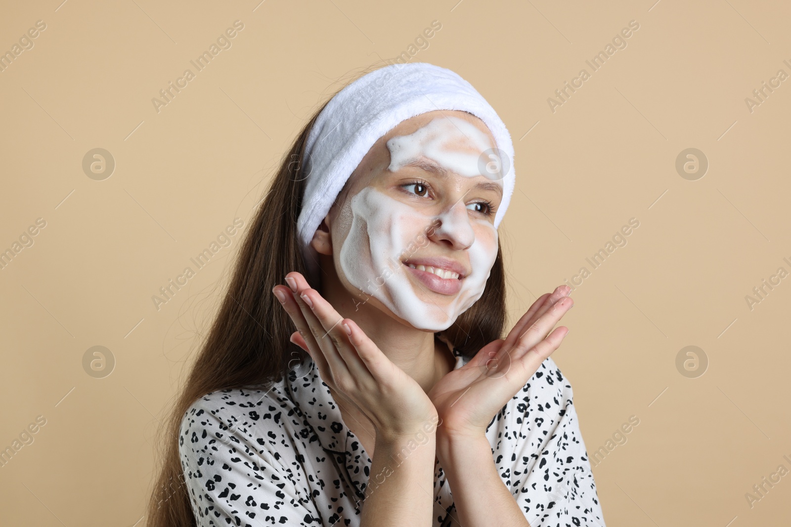 Photo of Teenage girl with cleansing foam on her face against beige background. Acne treatment