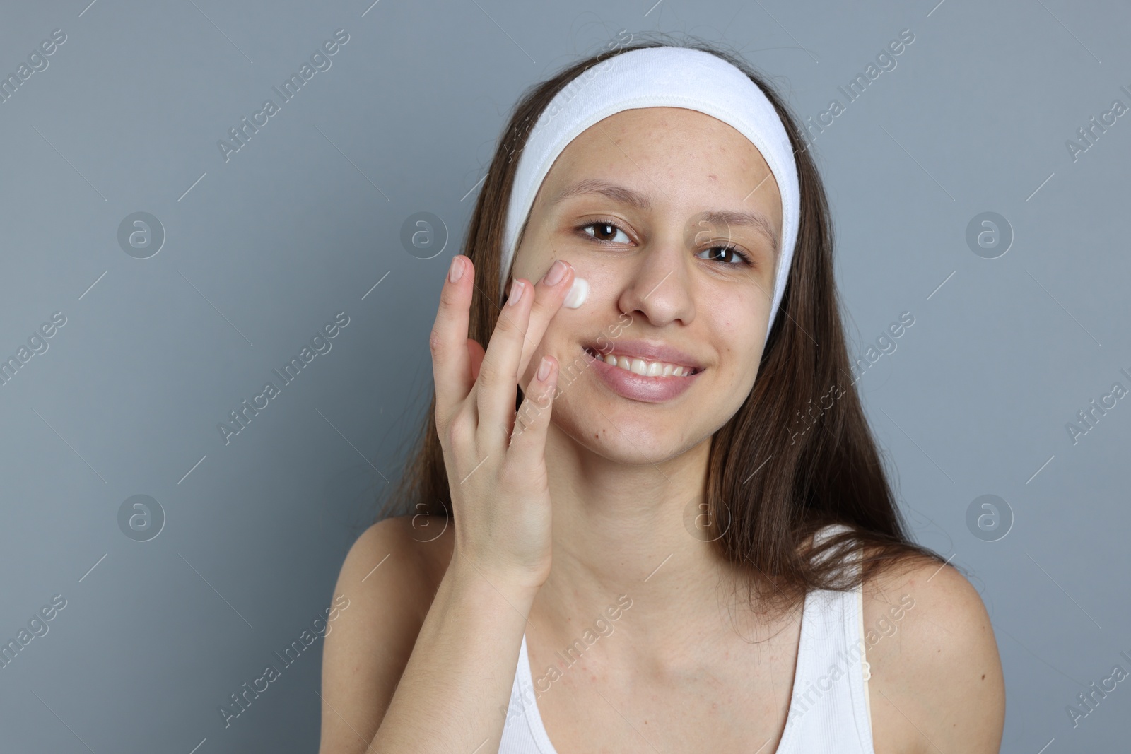 Photo of Teenage girl with acne problem applying cream on grey background