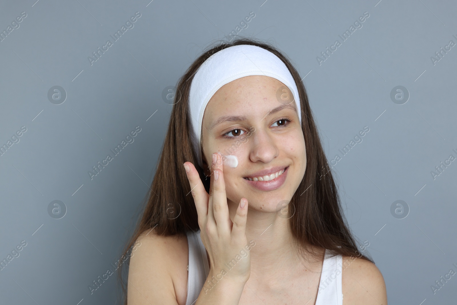 Photo of Teenage girl with acne problem applying cream on grey background