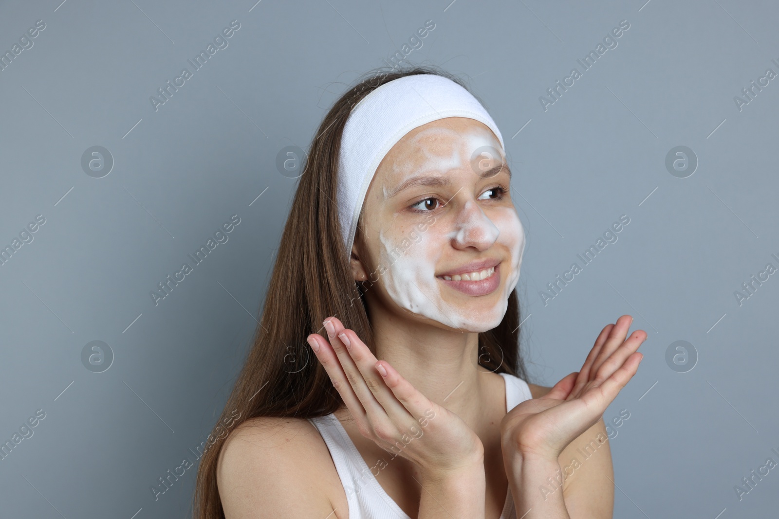 Photo of Teenage girl with cleansing foam on her face against grey background. Acne treatment