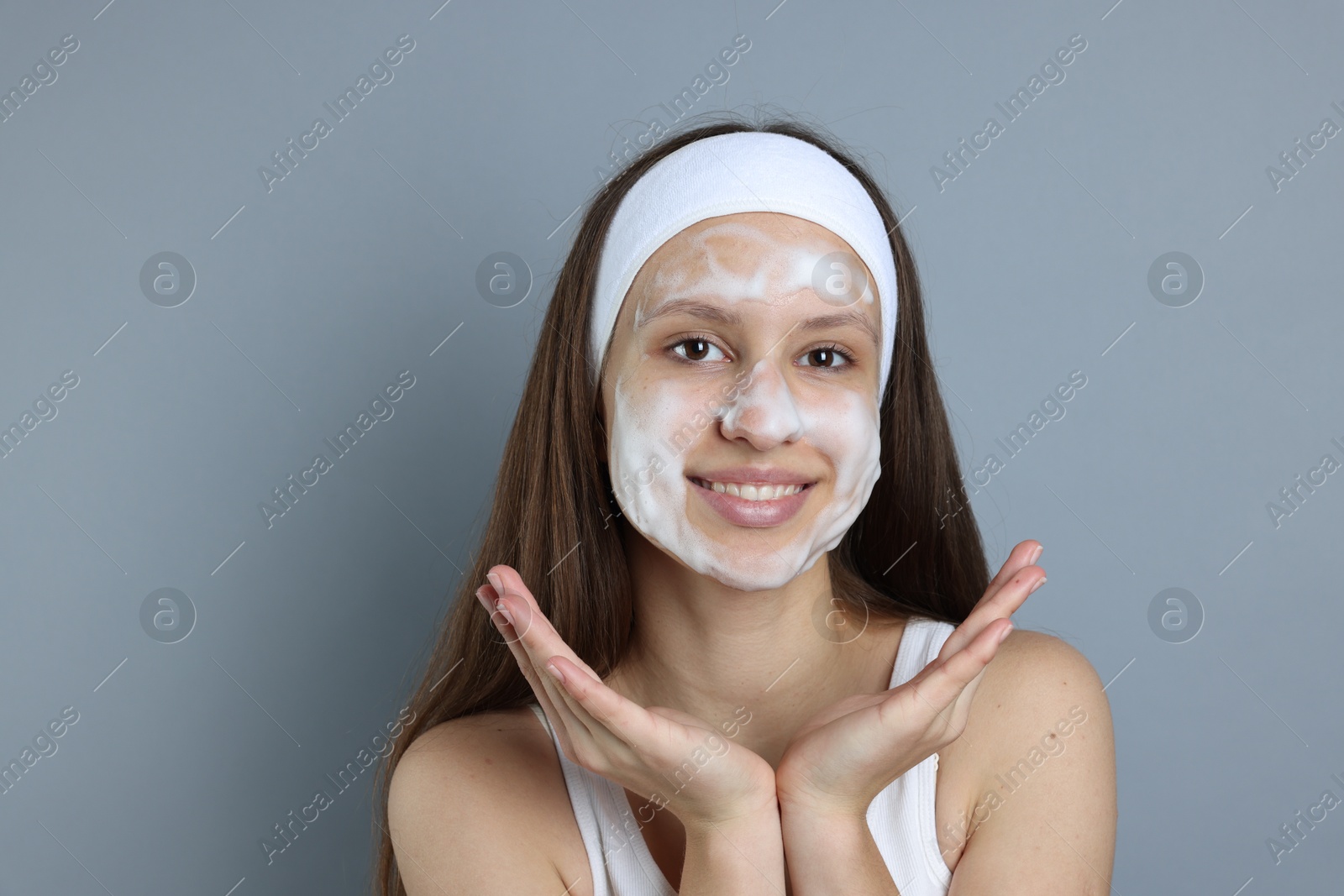 Photo of Teenage girl with cleansing foam on her face against grey background. Acne treatment