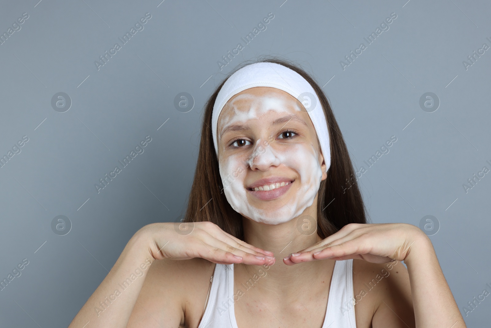 Photo of Teenage girl with cleansing foam on her face against grey background. Acne treatment