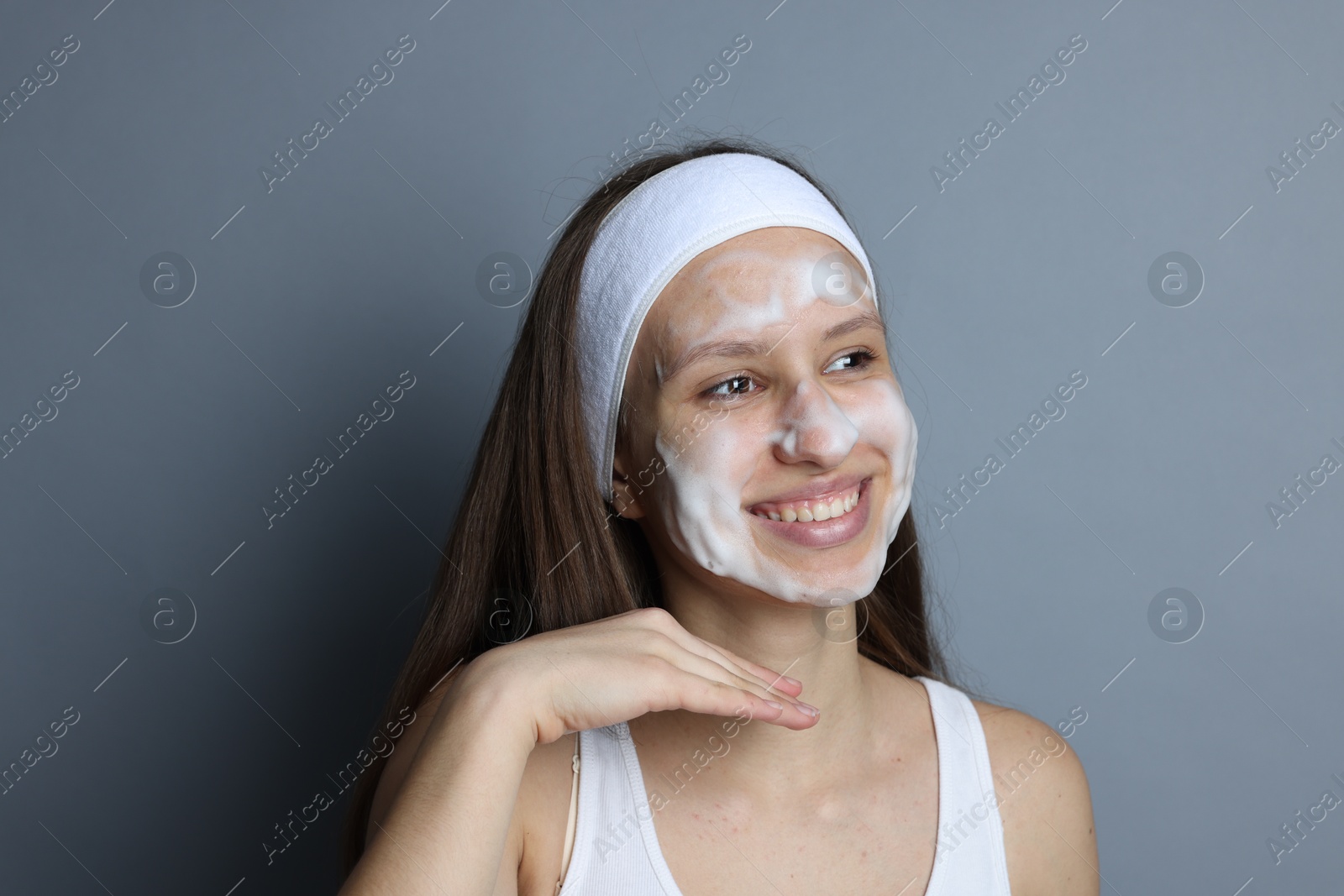 Photo of Teenage girl with cleansing foam on her face against grey background. Acne treatment