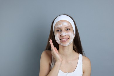 Photo of Teenage girl with cleansing foam on her face against grey background, space for text. Acne treatment