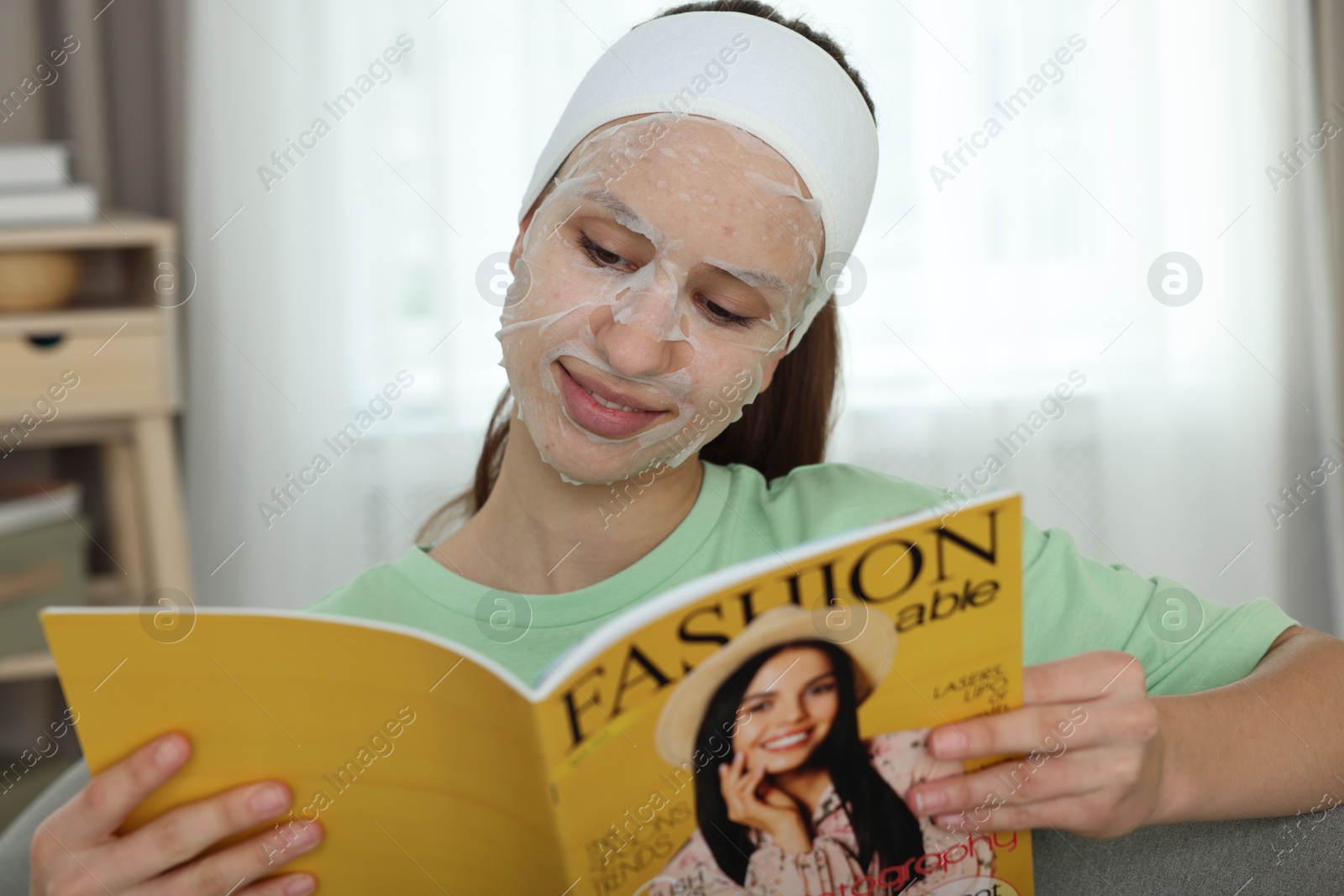 Photo of Teenage girl with sheet facial mask reading magazine at home. Acne treatment