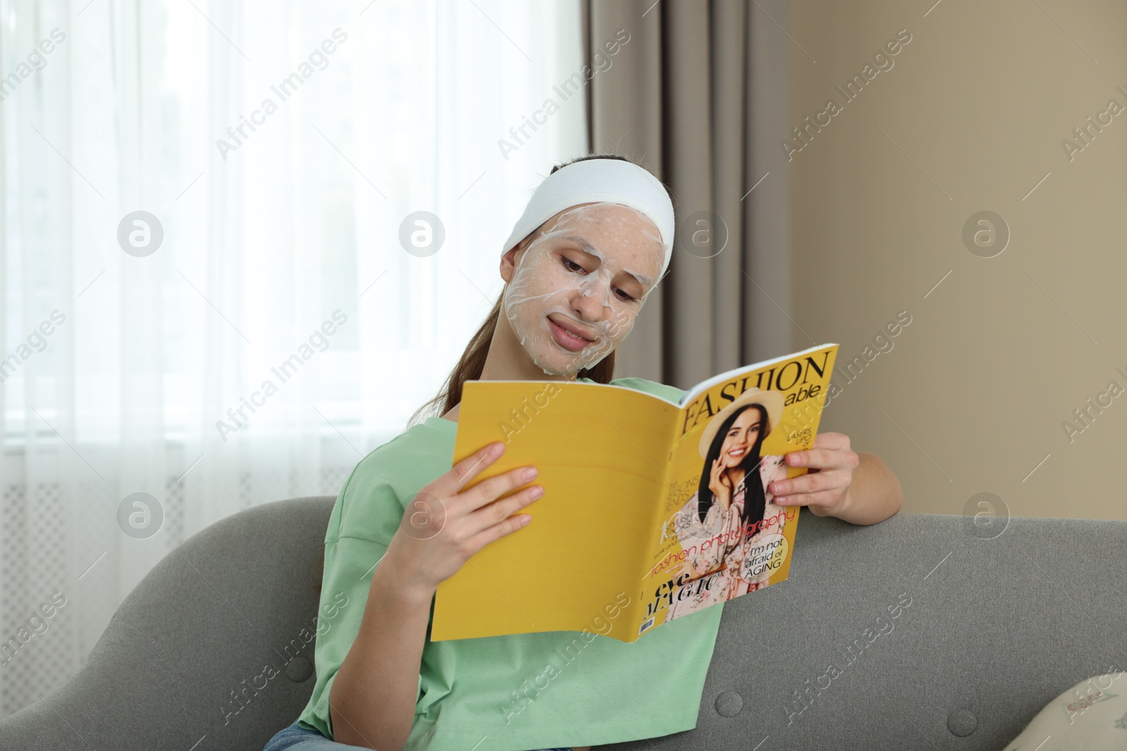 Photo of Teenage girl with sheet facial mask reading magazine at home. Acne treatment