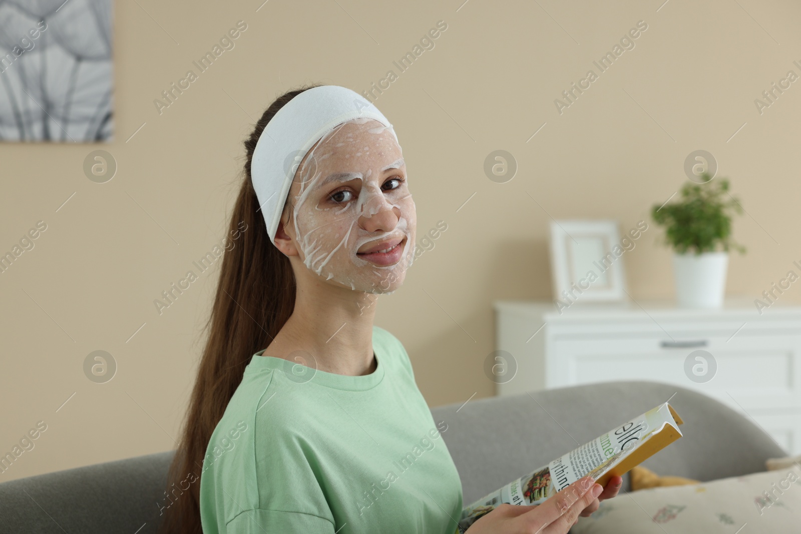 Photo of Teenage girl with sheet facial mask reading magazine at home. Acne treatment