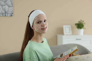 Photo of Teenage girl with sheet facial mask reading magazine at home. Acne treatment