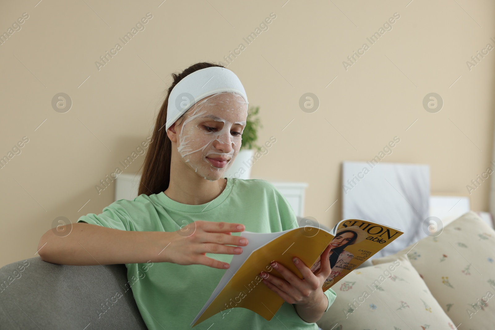 Photo of Teenage girl with sheet facial mask reading magazine at home. Acne treatment