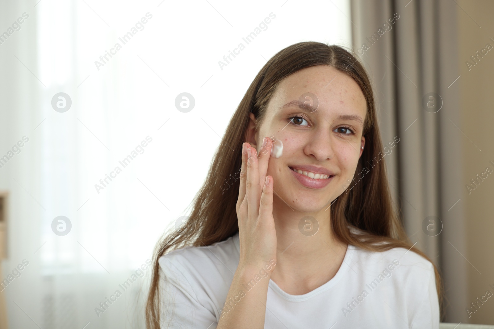 Photo of Teenage girl applying cream onto face at home, space for text. Acne treatment