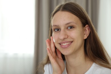 Photo of Teenage girl applying cream onto face at home, space for text. Acne treatment