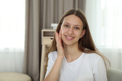 Photo of Teenage girl applying cream onto face at home, space for text. Acne treatment