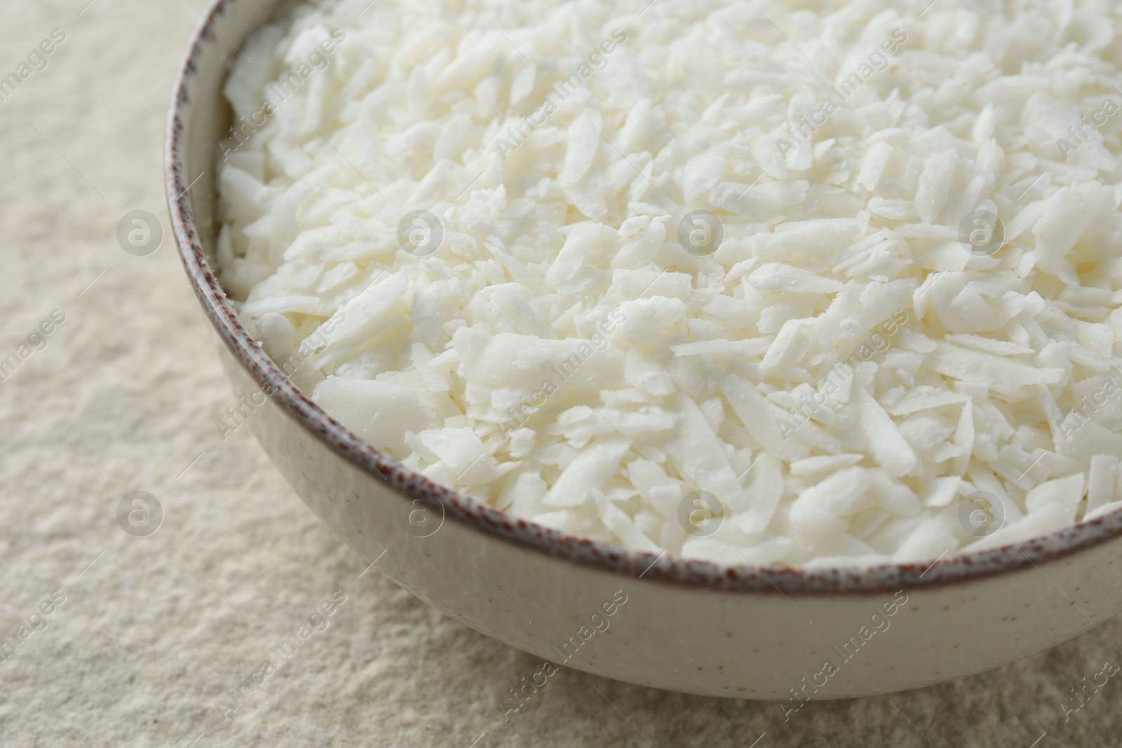 Photo of Soy wax in bowl on white textured table, closeup