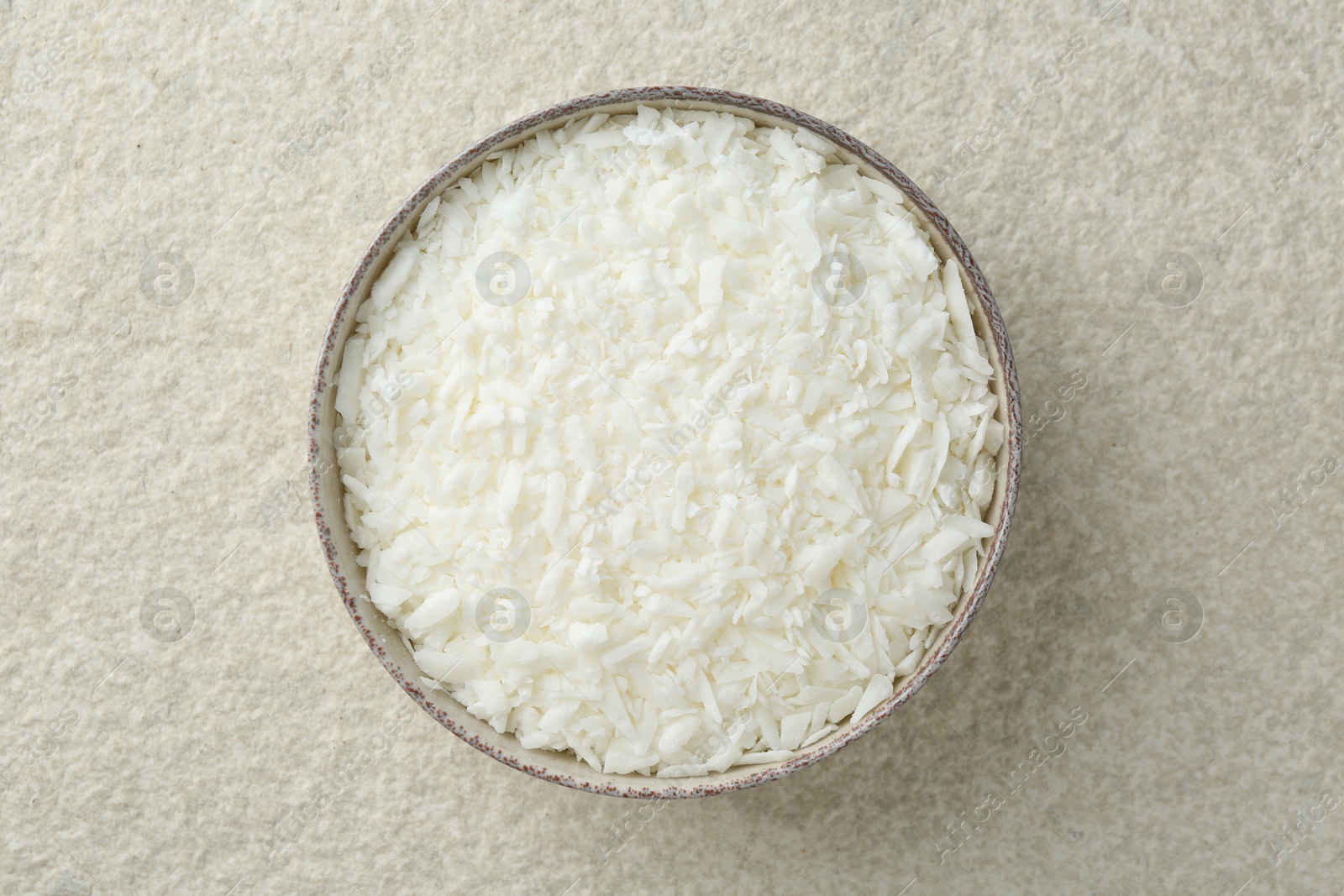 Photo of Soy wax in bowl on white textured table, top view