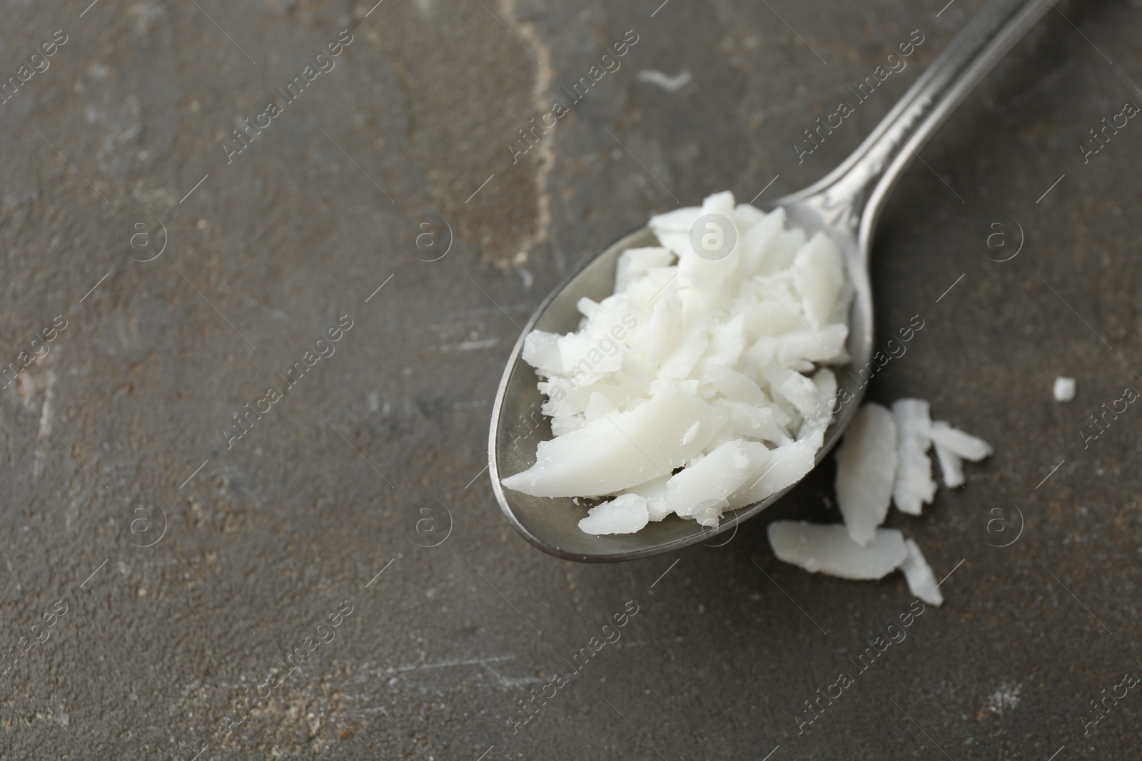 Photo of Soy wax in spoon on grey table, top view