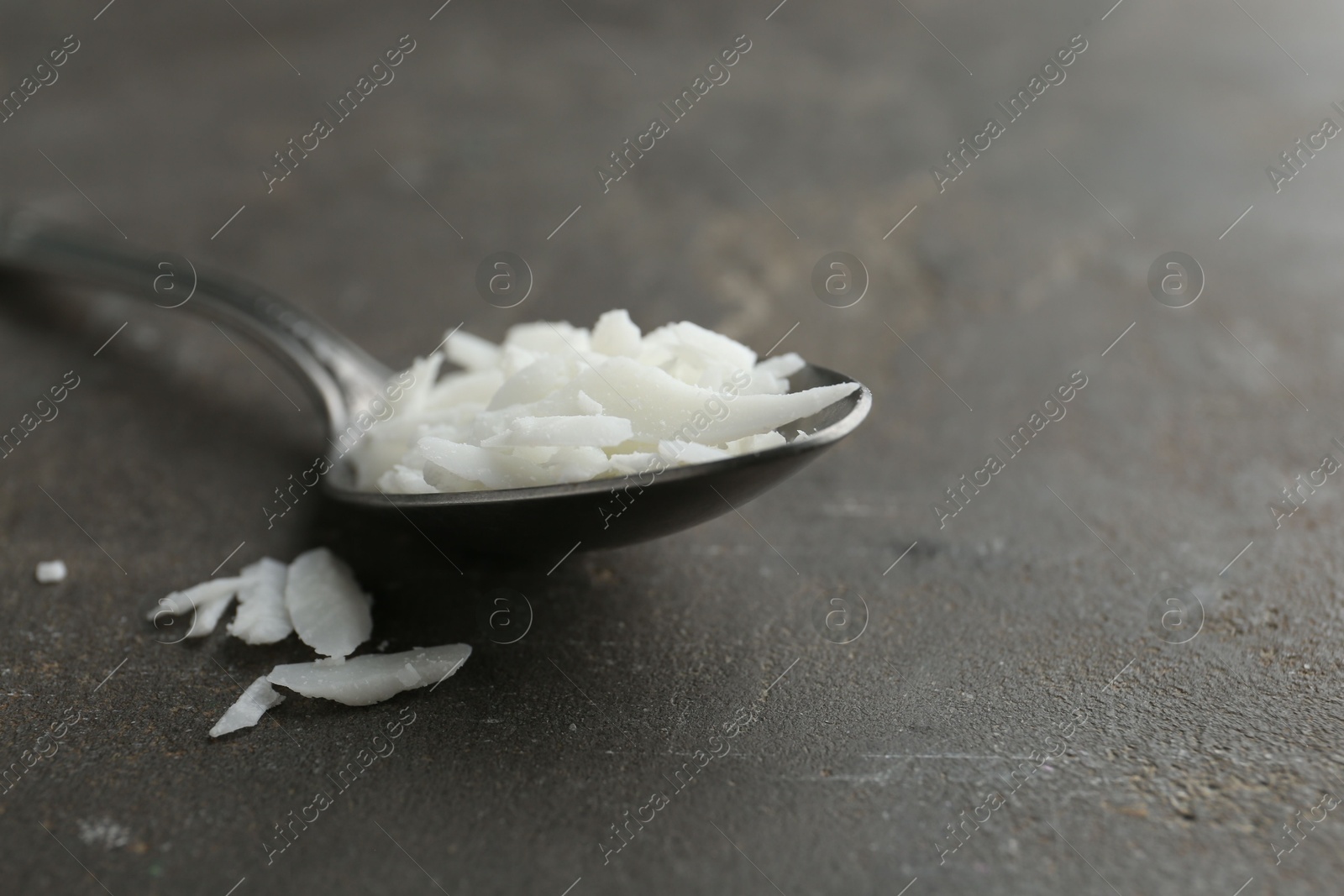 Photo of Soy wax in spoon on grey table, closeup. Space for text