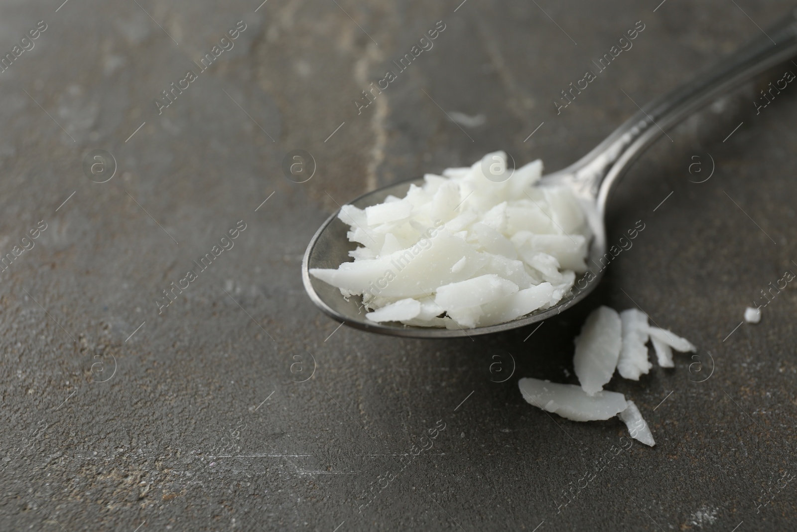 Photo of Soy wax in spoon on grey table, closeup. Space for text