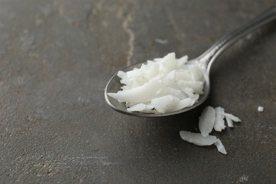 Photo of Soy wax in spoon on grey table, closeup. Space for text