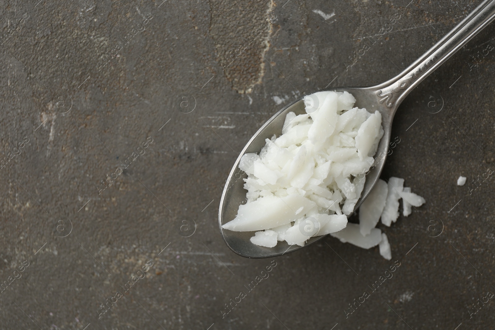 Photo of Soy wax in spoon on grey table, top view