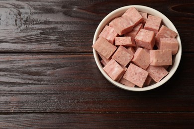 Photo of Pieces of canned meat in bowl on wooden table, top view. Space for text