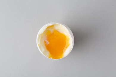 Soft boiled egg in cup on light grey background, top view