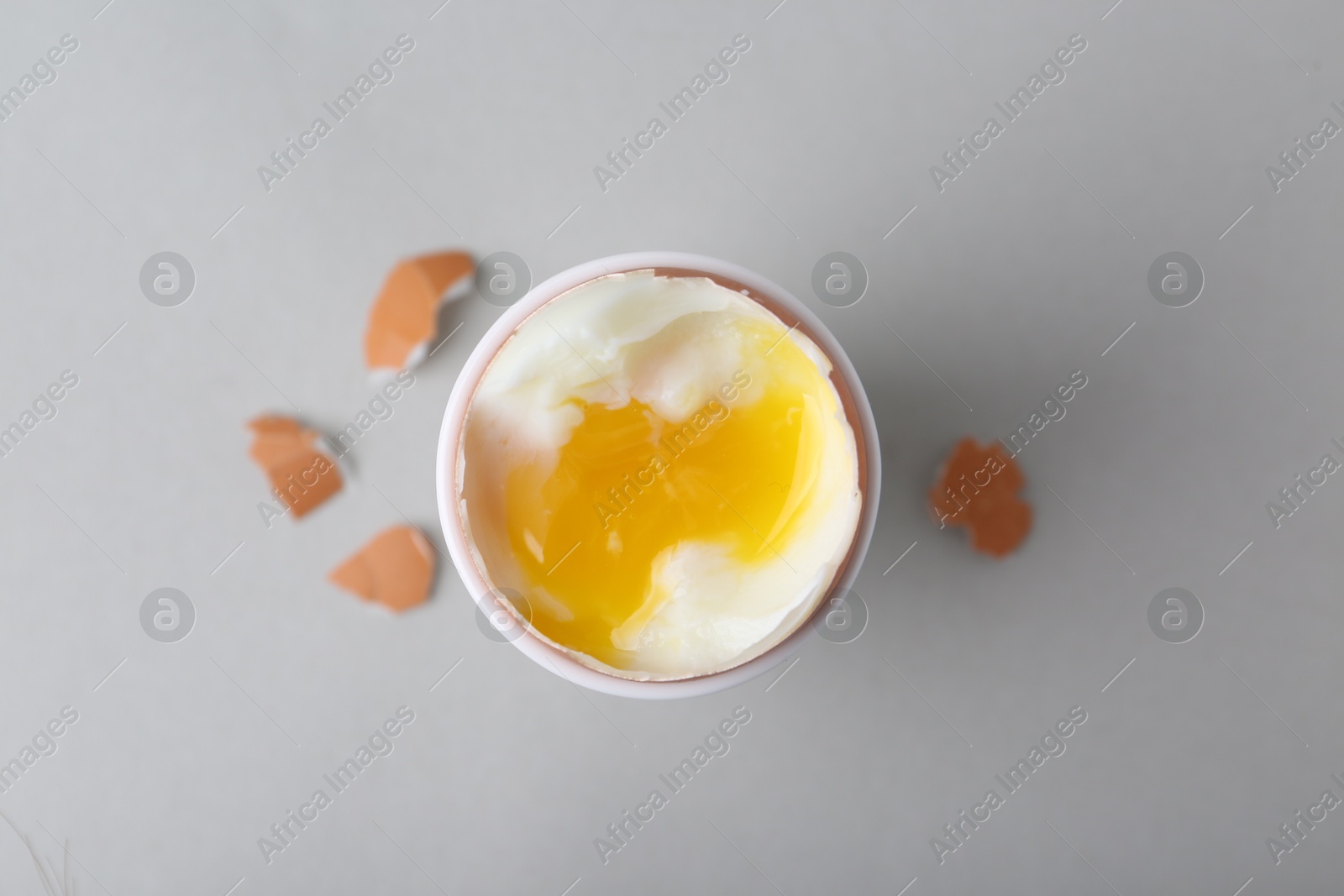 Photo of Soft boiled egg in cup and eggshell on light grey background, top view