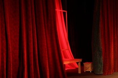 Photo of Elegant red curtains, table and frame on stage in theatre