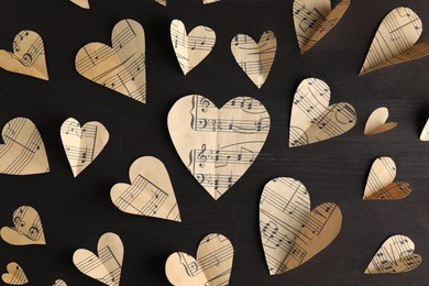 Paper hearts with notes on black wooden table, flat lay