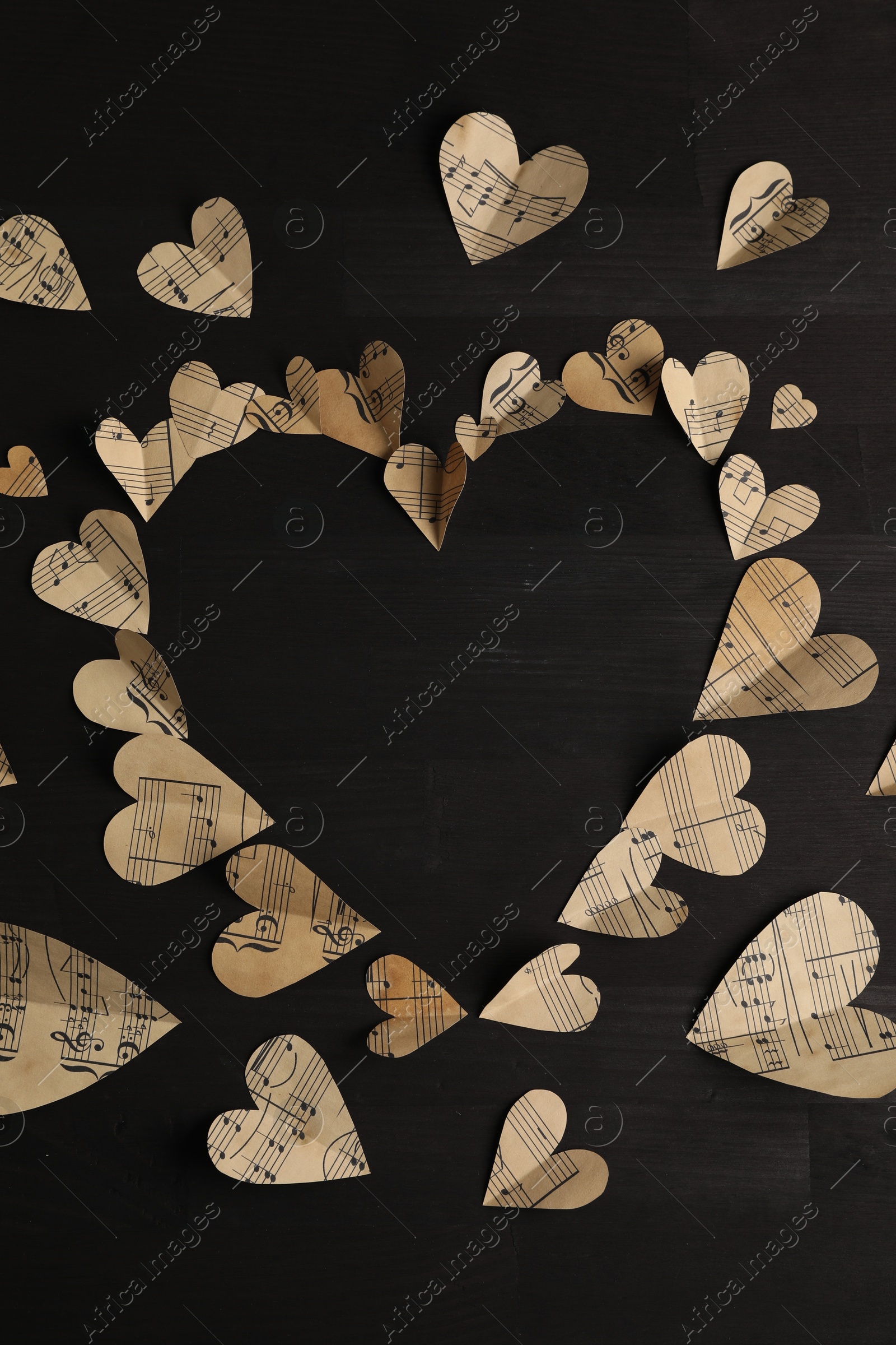 Photo of Heart shaped frame made of paper hearts with notes on black wooden table, top view. Space for text