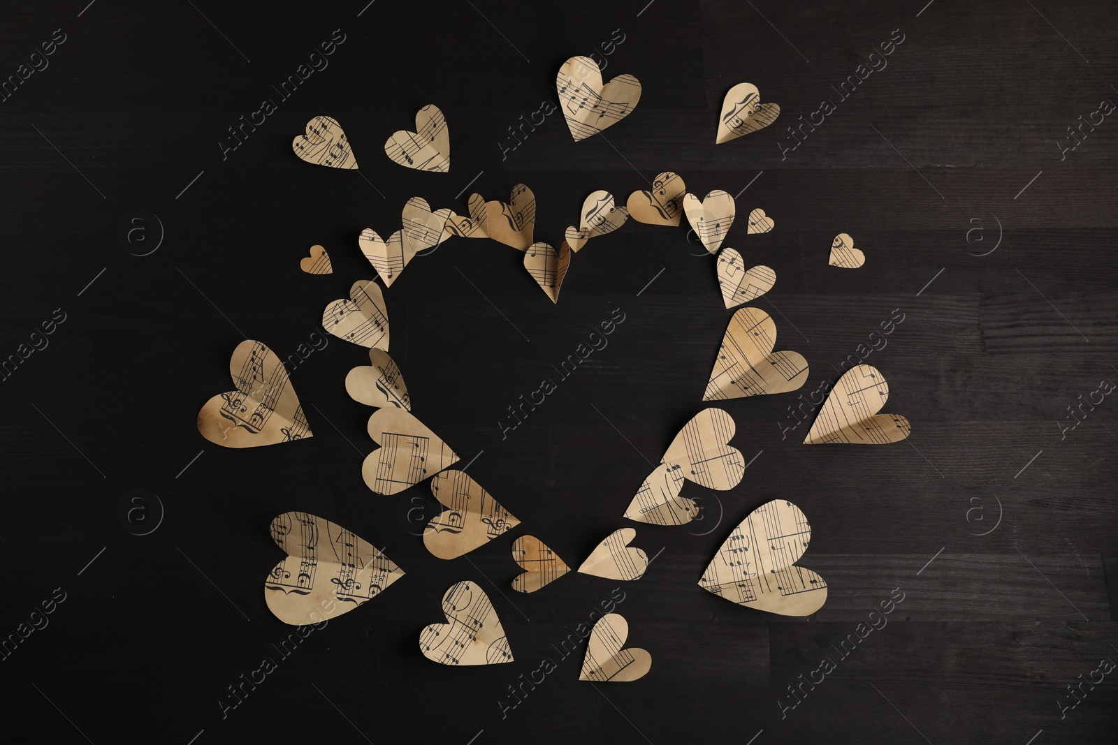 Photo of Heart shaped frame made of paper hearts with notes on black wooden table, top view. Space for text