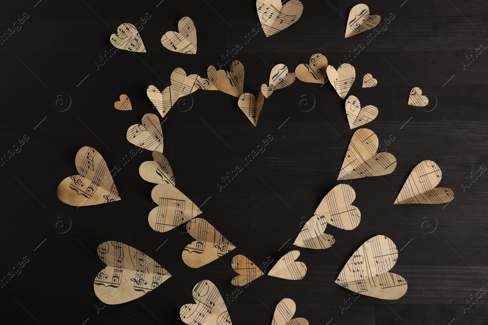 Photo of Heart shaped frame made of paper hearts with notes on black wooden table, top view. Space for text