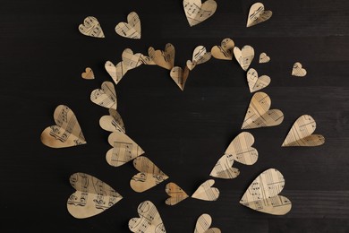 Heart shaped frame made of paper hearts with notes on black wooden table, top view. Space for text