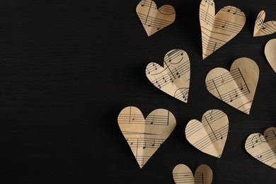 Paper hearts with notes on black wooden table, flat lay. Space for text