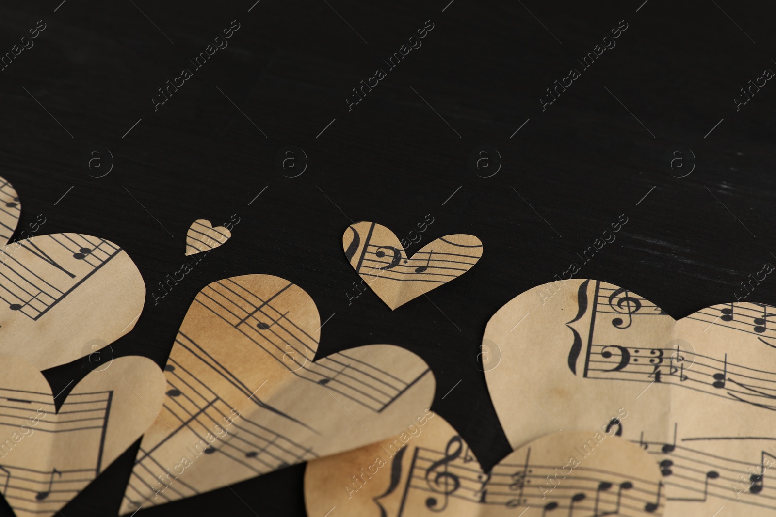 Photo of Paper hearts with notes on black wooden table, closeup. Space for text