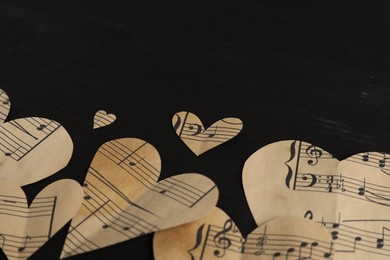 Photo of Paper hearts with notes on black wooden table, closeup. Space for text