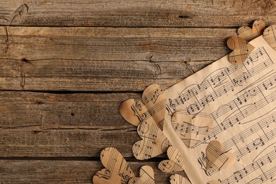 Paper hearts with notes and musical note sheet on wooden table, flat lay. Space for text