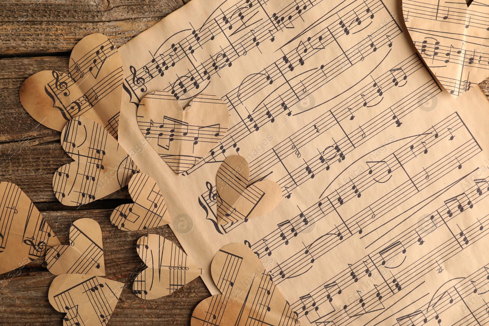 Photo of Paper hearts with notes and musical note sheet on wooden table, flat lay