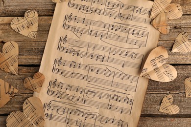 Photo of Paper hearts with notes and musical note sheet on wooden table, flat lay