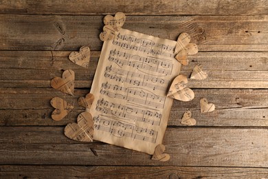 Paper hearts with notes and musical note sheet on wooden table, flat lay