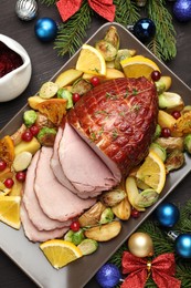 Photo of Tasty baked ham served with vegetables and oranges on black wooden table, flat lay