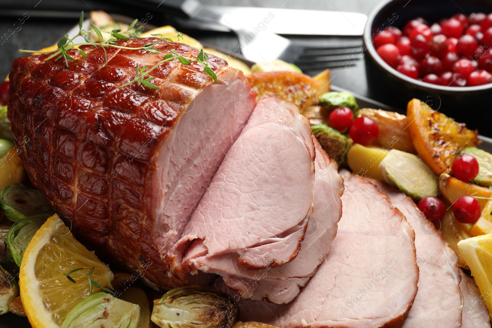 Photo of Tasty baked ham served with vegetables and oranges on black table, closeup