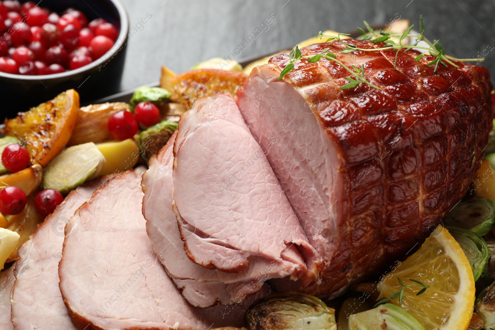 Photo of Tasty baked ham served with vegetables and oranges on black table, closeup