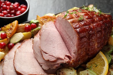 Tasty baked ham served with vegetables and oranges on black table, closeup