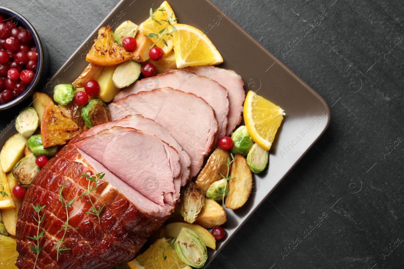 Photo of Tasty baked ham served with vegetables and oranges on black table, top view